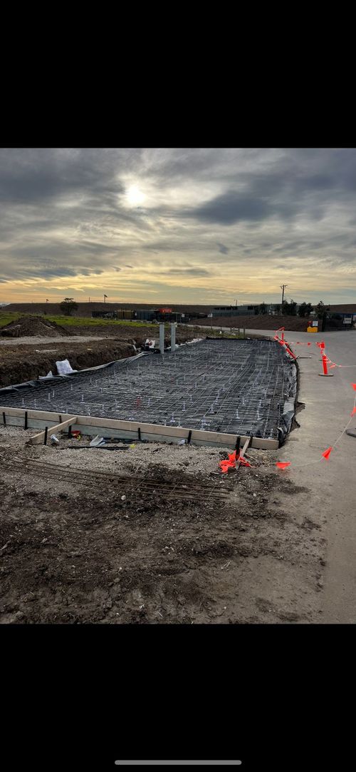 Construction site with concrete foundation framework, surrounded by safety barriers, under a cloudy sky.