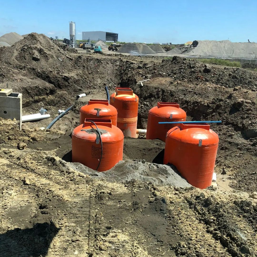 Five large orange tanks sit partially buried in dirt at a construction site.