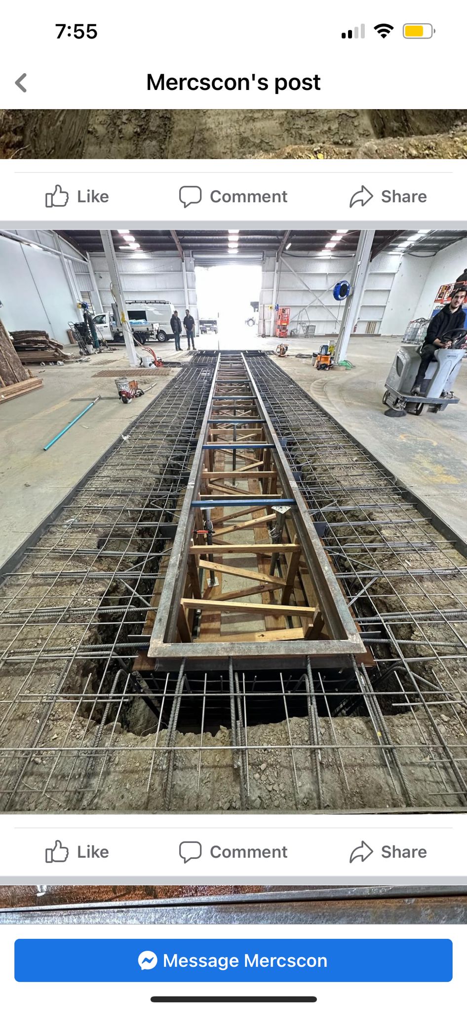 Steel framework being constructed in a large industrial warehouse with workers in the background.