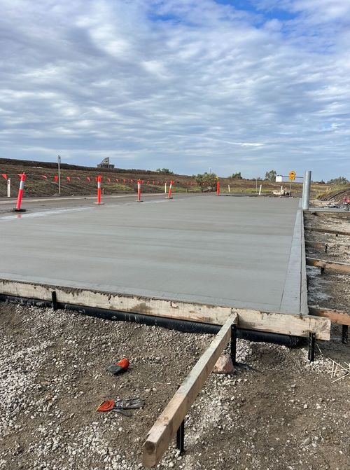 Freshly poured concrete slab with orange safety cones around it on a construction site.