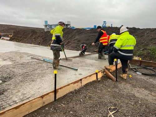 Workers in high-visibility gear smooth wet concrete on a construction site with tools.